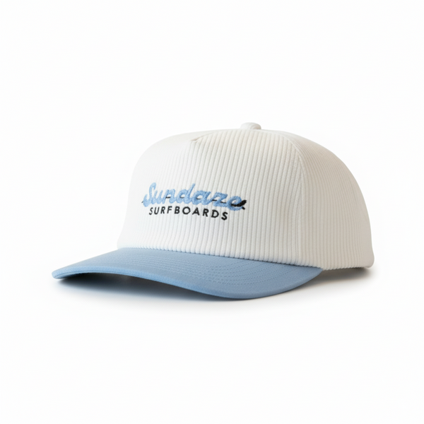 White and blue cap with sundaze Surfboards' logo on a wooden surface.